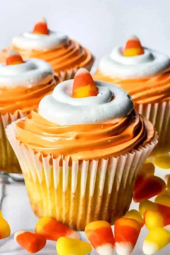 Four cupcakes with orange and white icing and topped with a candy corn piece. 