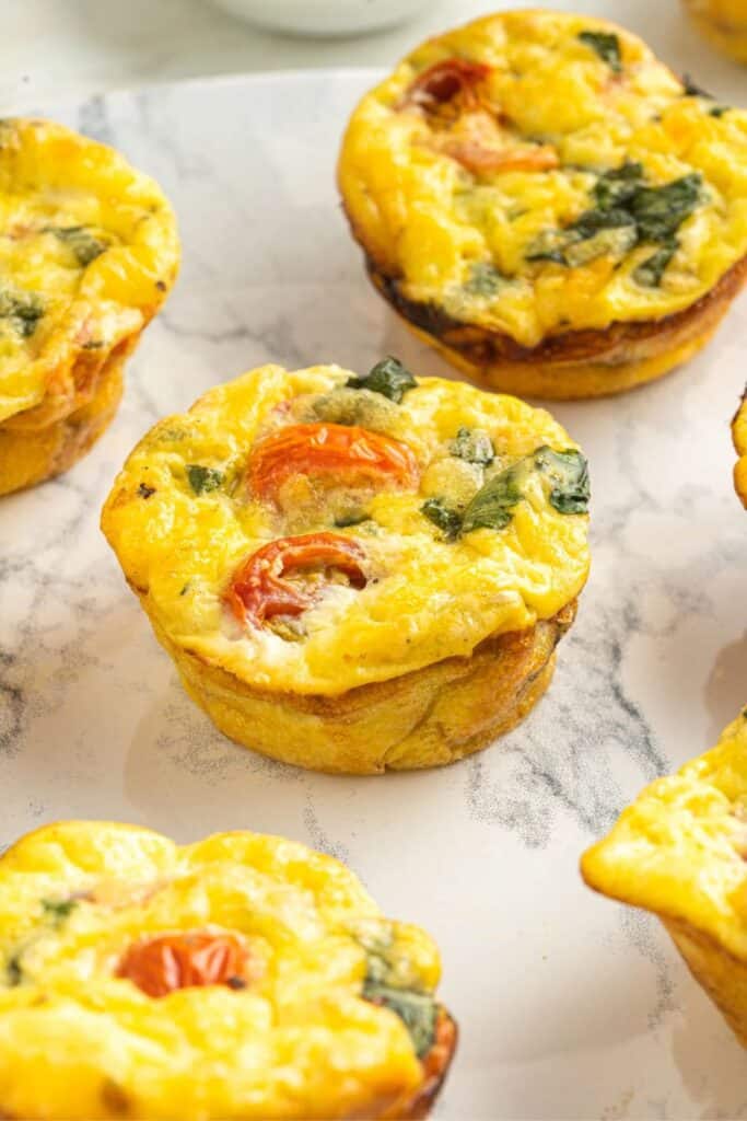 Close-up of freshly baked caprese egg muffins on a marble surface, filled with cherry tomatoes, wilted spinach, and melted cheese.