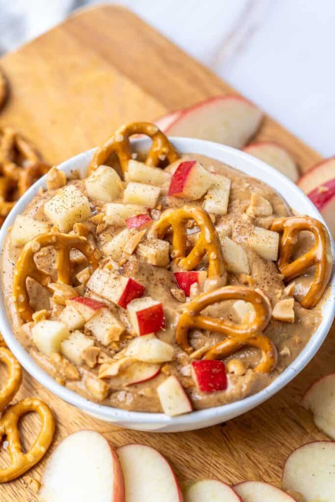 Bowl of caramel creemcheese dip with cubes of apple and pretzels stuck on top. 