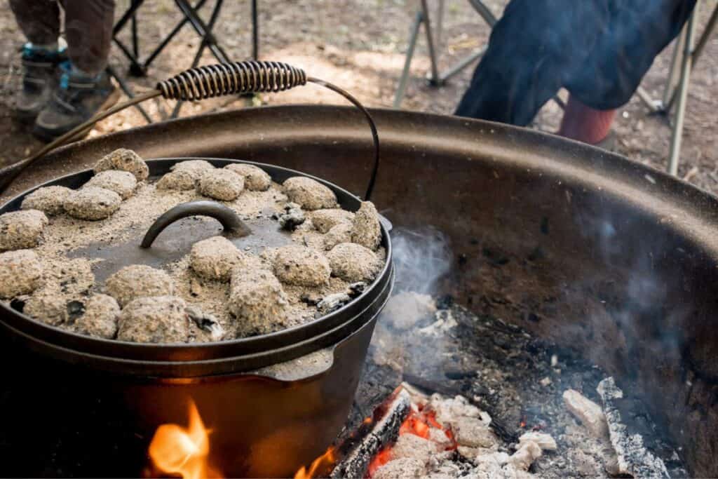 Cast-Iron Dutch Oven pot in a campfire with coals on top.