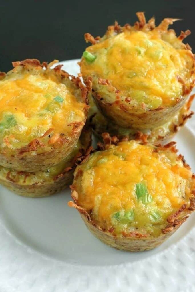 Cheddar onion hashbrown cups with crispy golden potato edges and melted cheese on top garnished with green onions.