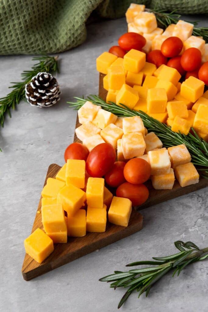 Cheese cube Christmas platter in in the shape of a tree, with cherry tomatoes, cheese cubes  and rosemary sprigs in  rows. 