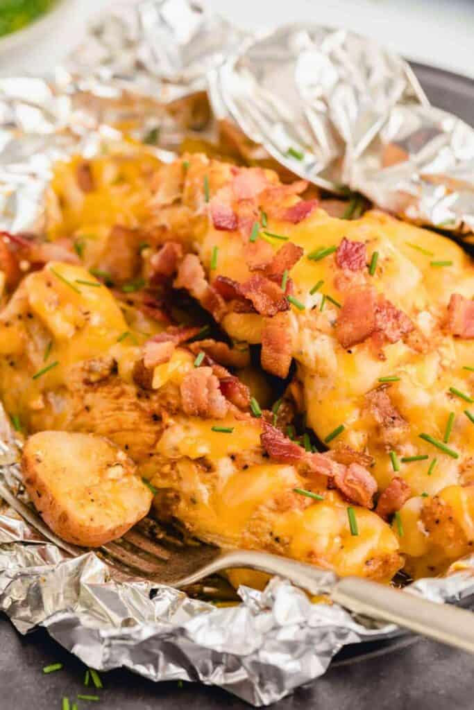 A foil pouch filled with chicken breast, melted cheese , bacon and potatoes. 