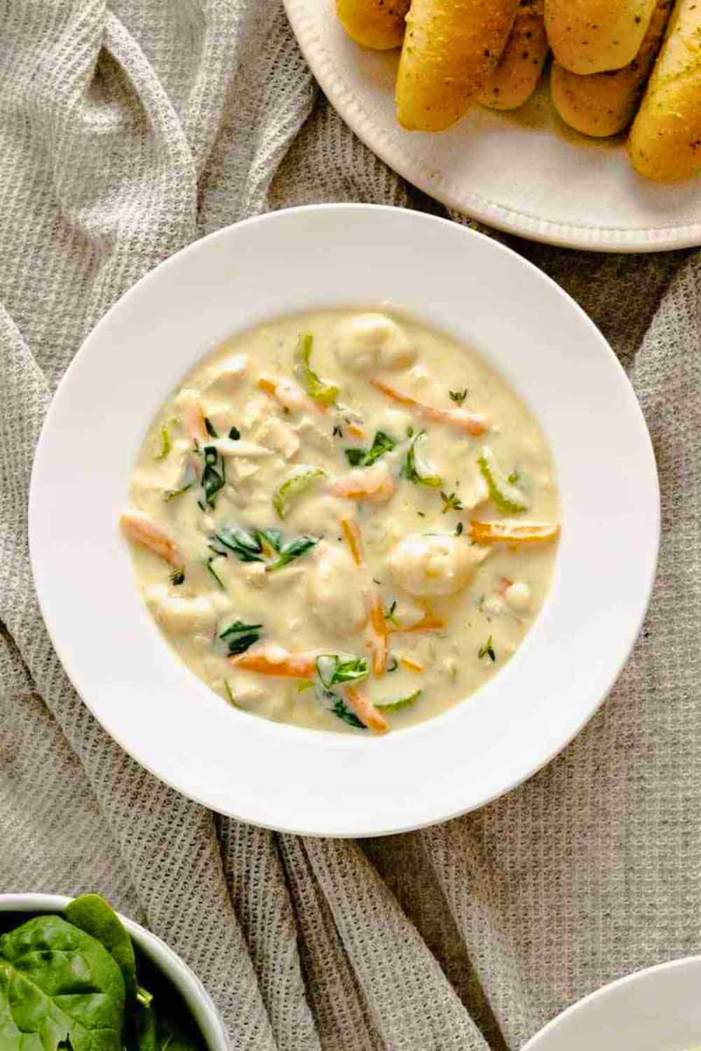 Chicken and gnocchi soup with tender chicken pillowy gnocchi carrots celery and spinach is served in a creamy broth. The comforting soup is shown alongside golden breadsticks.