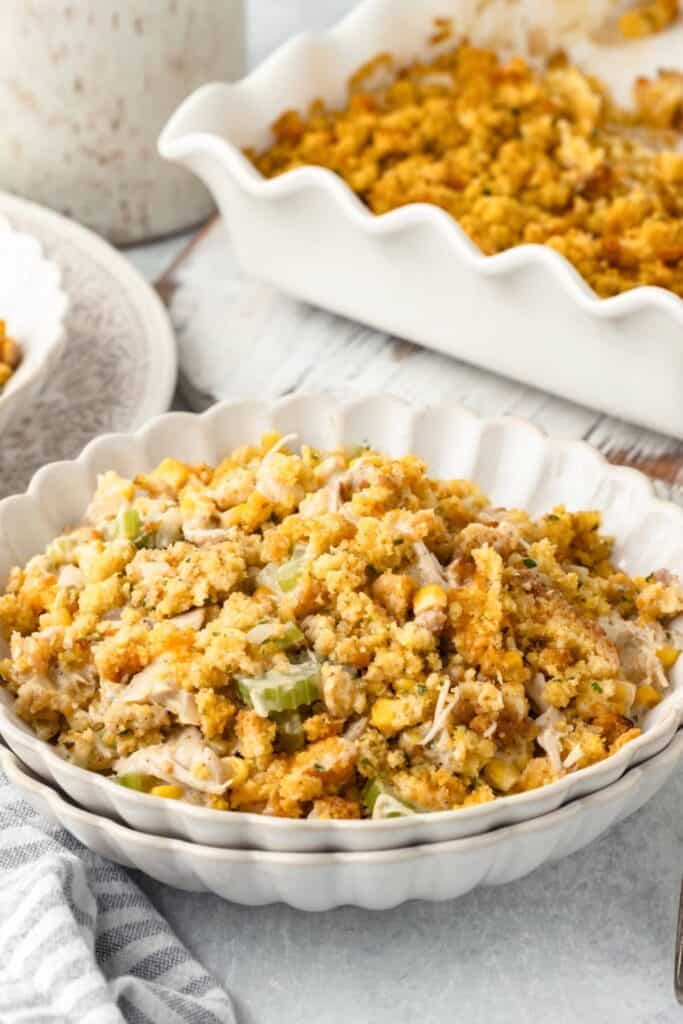 Chicken and stuffing bake with shredded chicken, golden seasoned stuffing, celery and corn served in a white bowl beside the casserole dish.