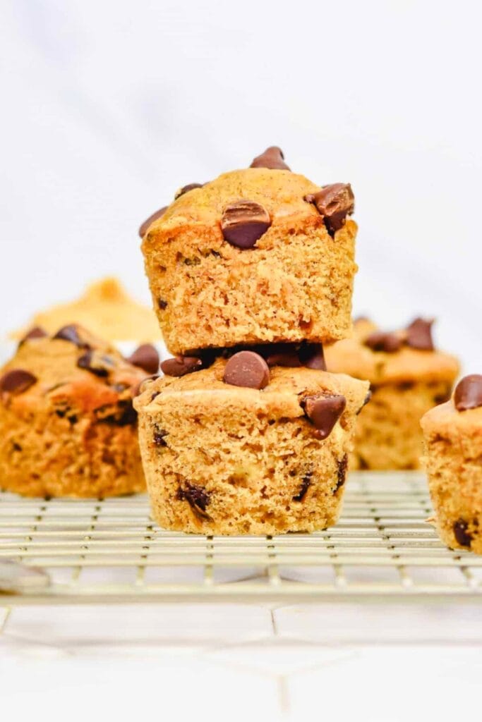 Golden chocolate chip peanut butter muffins stacked on a cooling rack, with melted chocolate chips visible on top and throughout the soft, moist crumb. The muffins have a slightly crisp exterior and a tender center, combining classic peanut butter flavor with rich chocolate.