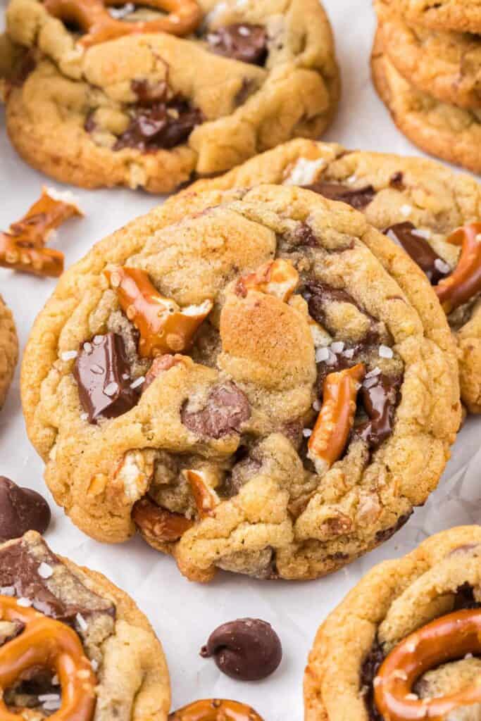 Thick chocolate chip pretzel cookies with large chunks of melted chocolate, broken pretzel pieces, and flakes of sea salt baked into a golden brown cookie. The close up view highlights the soft texture and sweet salty combination of chocolate and pretzels.