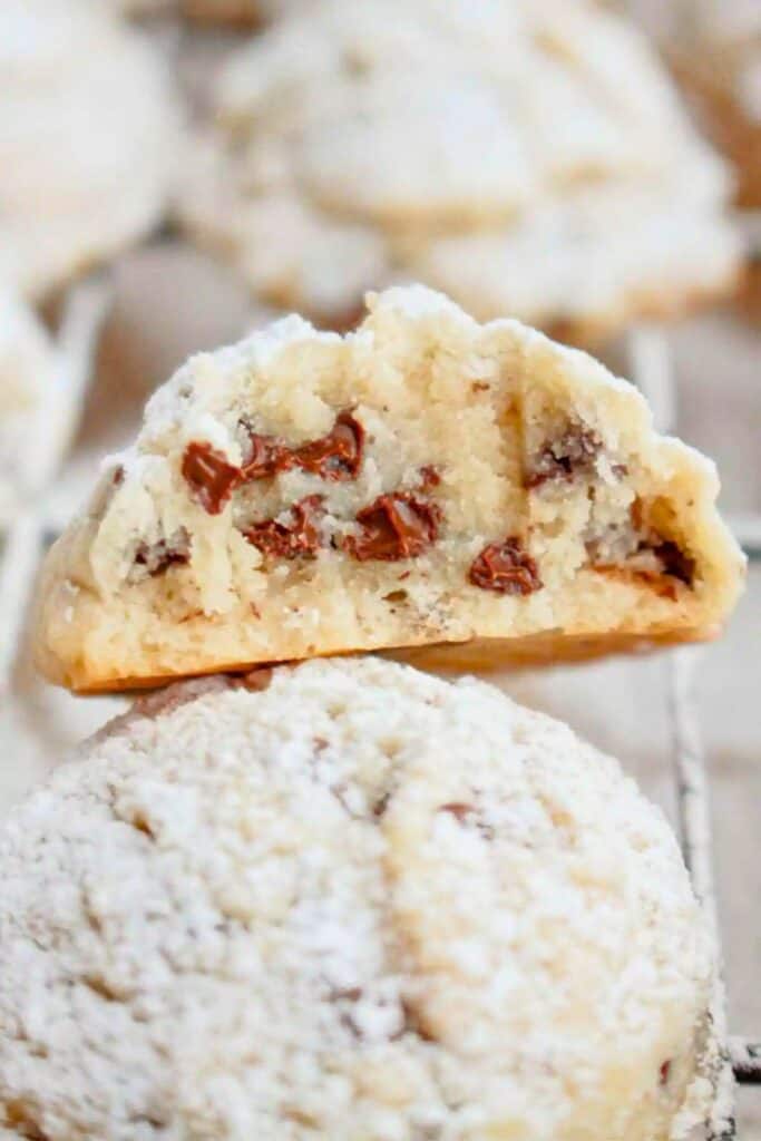 Close-up of a chocolate chip snowball cookie coated in powdered sugar, with one cookie split open to reveal its soft, buttery interior filled with gooey chocolate chips.