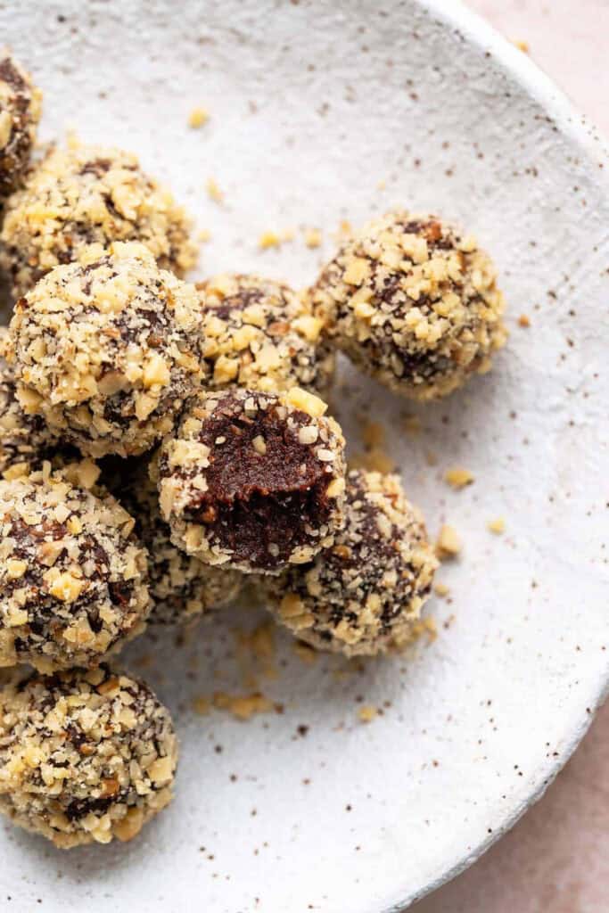 A plate of round chocolate date balls rolled in nuts. 