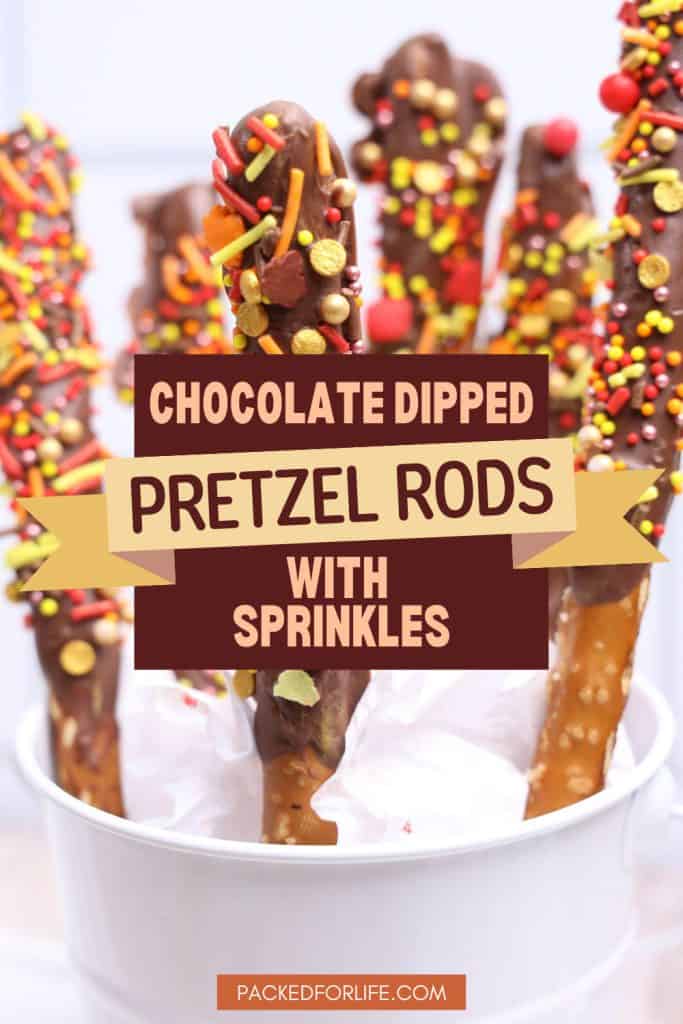 A white cup holds tall chocolate covered pretzel rods coated with colorful red, yellow, and orange sprinkles, text reads "Chocolate dipped pretzel rods with sprinkles."