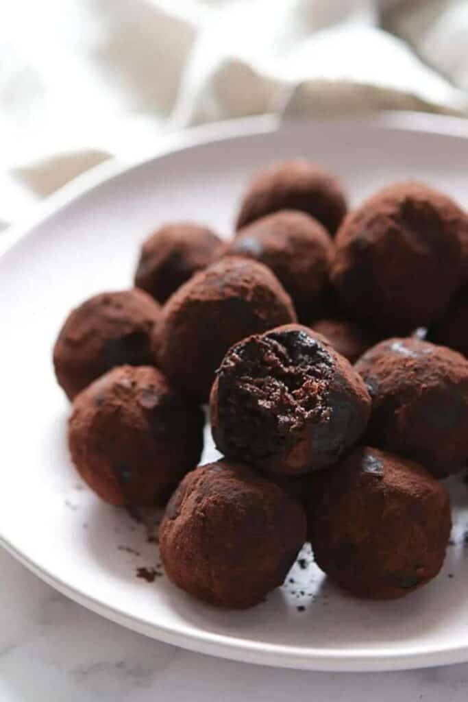 Plate piled with chocolate peanut butter balls with cocoa powder over top. 