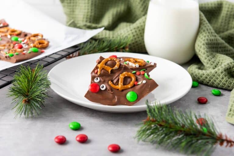 Piece of milk chocolate reindeer bark Christmas treats on a plate surrounded by fir branches and a glass bottle of milk.