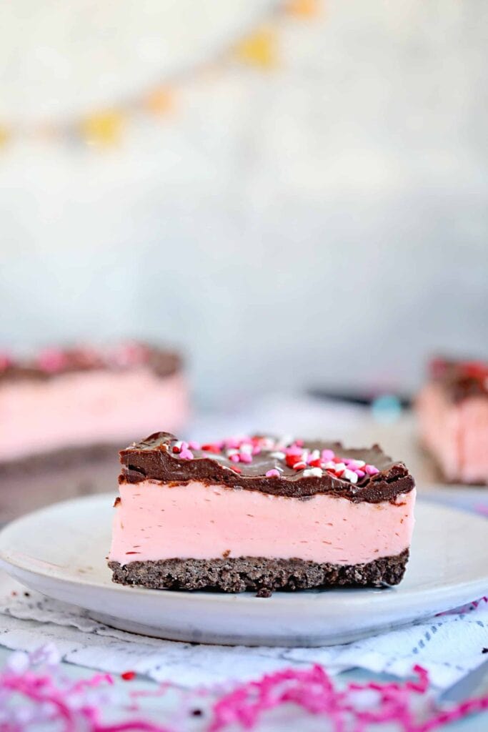 Close up of strawberry cheesecake bar topped with chocolate and Valentine's sprinkles. 