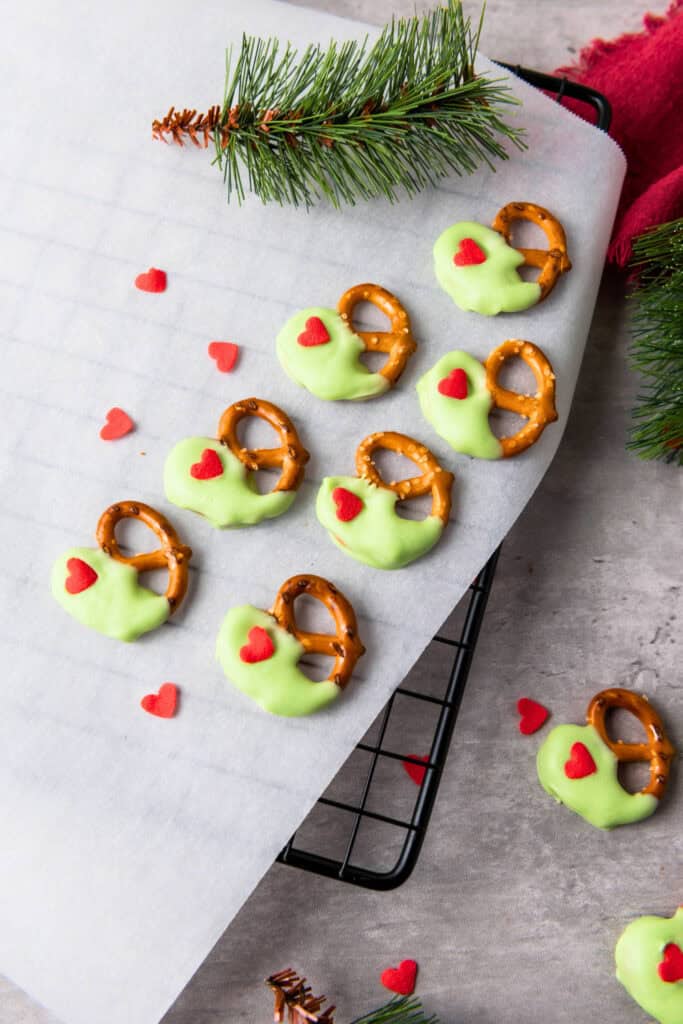 Green candy-dipped pretzels decorated with red heart sprinkles arranged on parchment paper, perfect as festive holiday pretzel treats for Christmas