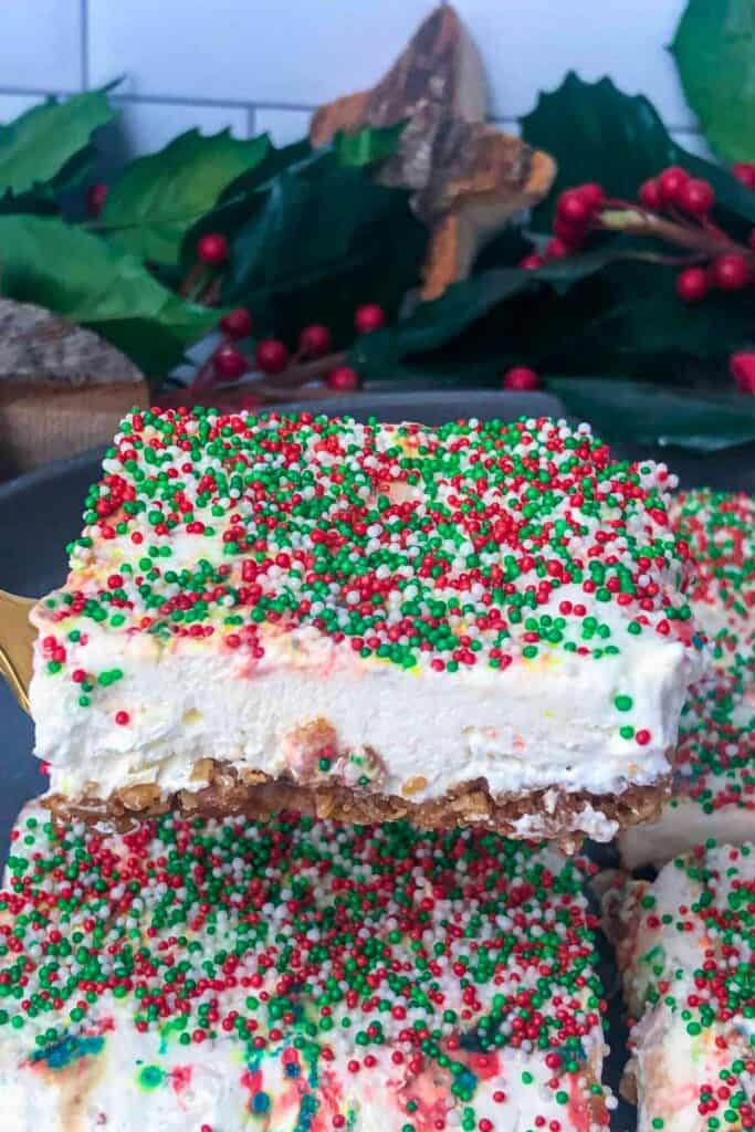 Close-up of no bake Christmas cheesecake crunch bars topped with red, green, and white sprinkles over a creamy cheesecake layer and crispy golden crust.