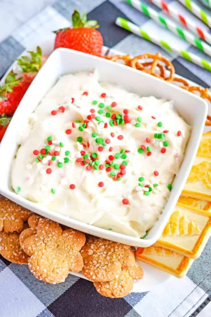 Square bowl of Christmas Cookie dip surrounded by pretzles, cookies and strawberries.