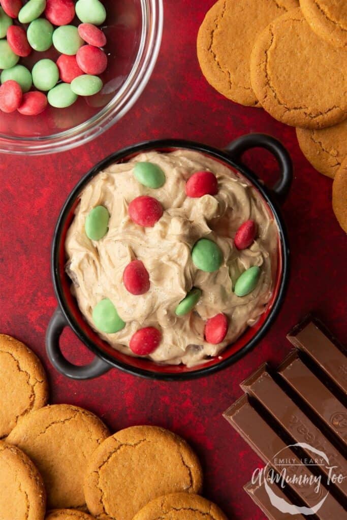 Small ceramic bowl of Christmas cookies dip topped with red and green candies, beside gingersnap cookies. 