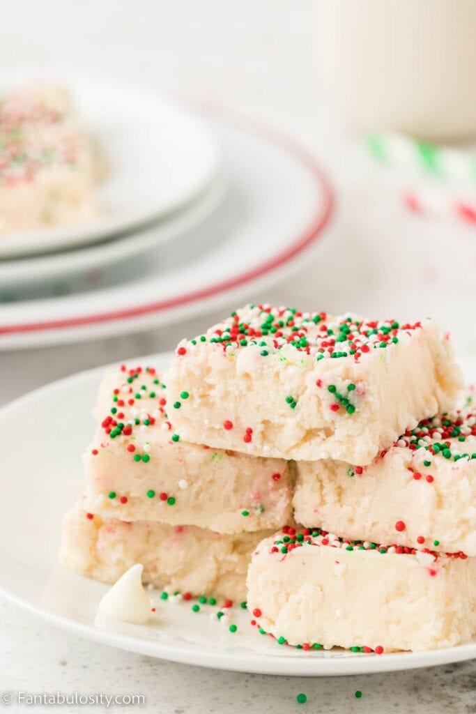 Stacked squares of creamy white cookie fudge topped with red, green, and white sprinkles, served on a white plate. 