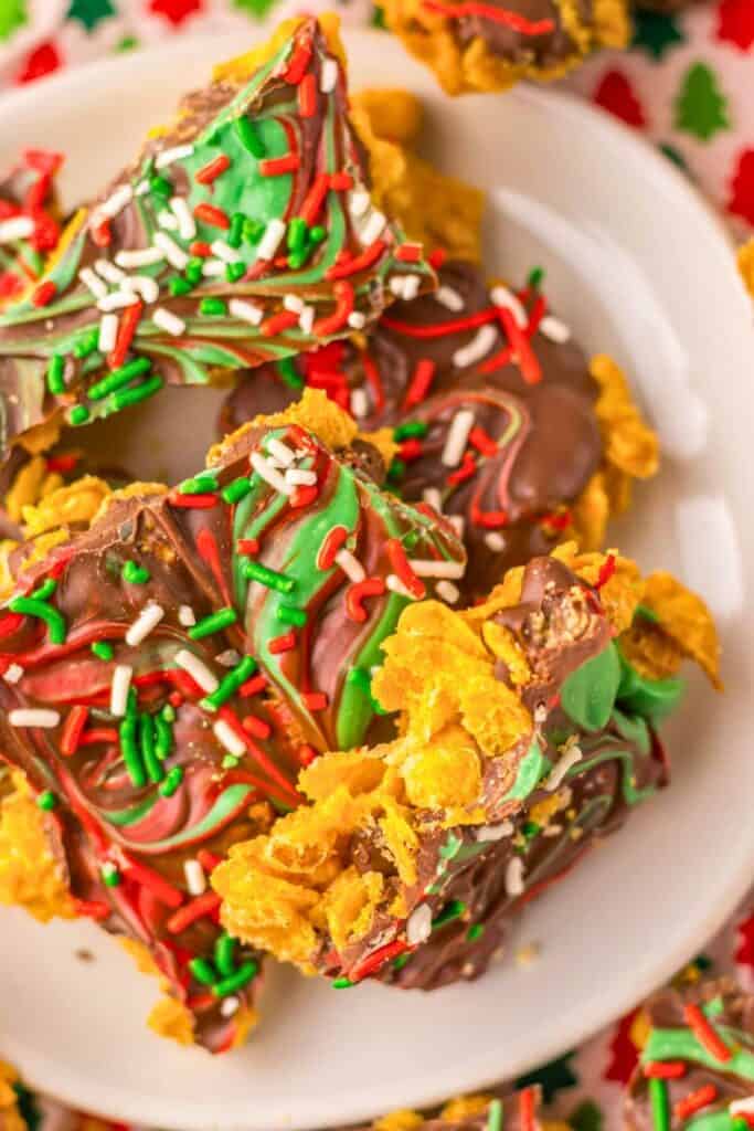 Close-up of colorful Christmas cornflake brittle made with swirls of red, green, and chocolate candy coating, topped with festive sprinkles and crispy cornflakes for a crunchy holiday treat.