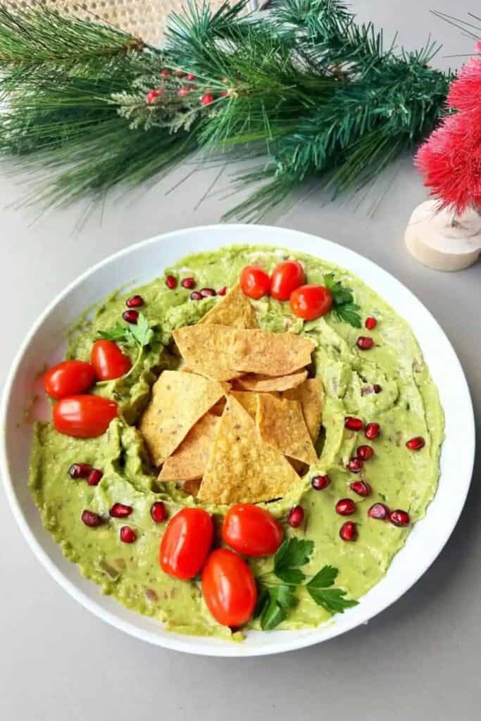 Bowl of Christmas Guacamole with pomegranate seeds and cherry tomotoes on top. 