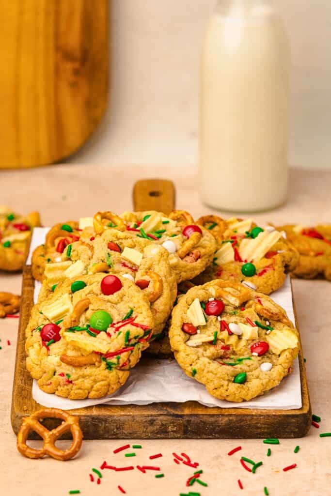 A wooden board piled with Christmas Kitchen Sink Cookies loaded with pretzels, red and green candies, white chocolate pieces, and festive sprinkles, an easy option for potluck dessert ideas.