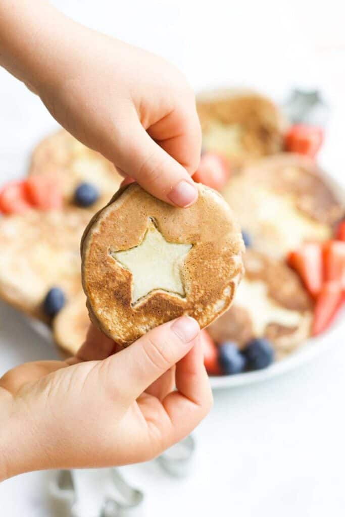 Kids hand holiding a pancake with a cute out star in the middle made of apple slice.