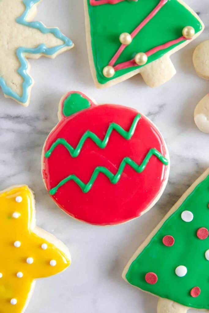 Colorfully decorated Christmas sugar cookies shaped like ornaments, stars, trees, and snowflakes are topped with smooth royal icing in festive shades of red, green, yellow, and blue.