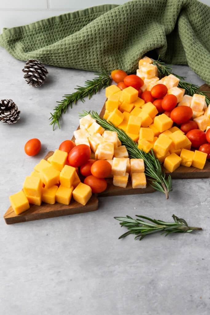 Side view of a Christmas tree shaped cubed cheese & cherry tomato board decorated with fresh rosemary sprigs.