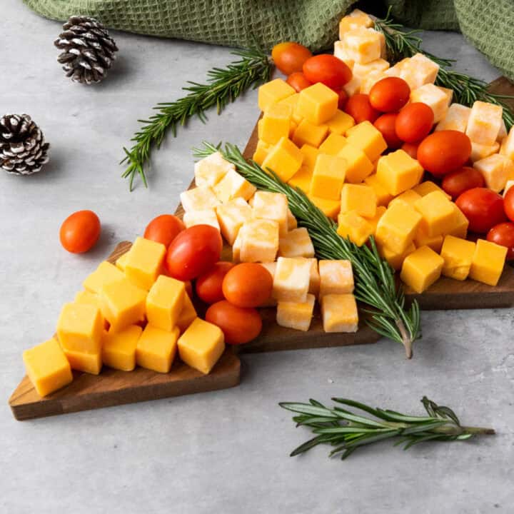 Side view of a Christmas tree shaped cubed cheese & cherry tomato board decorated with fresh rosemary sprigs.