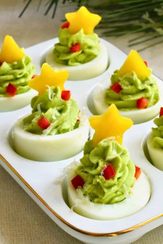Christmas tree appetizers made with hard boiled egg halves topped with piped green deviled egg filling. Diced red pepper decorates the trees like ornaments and yellow pepper stars top each one.