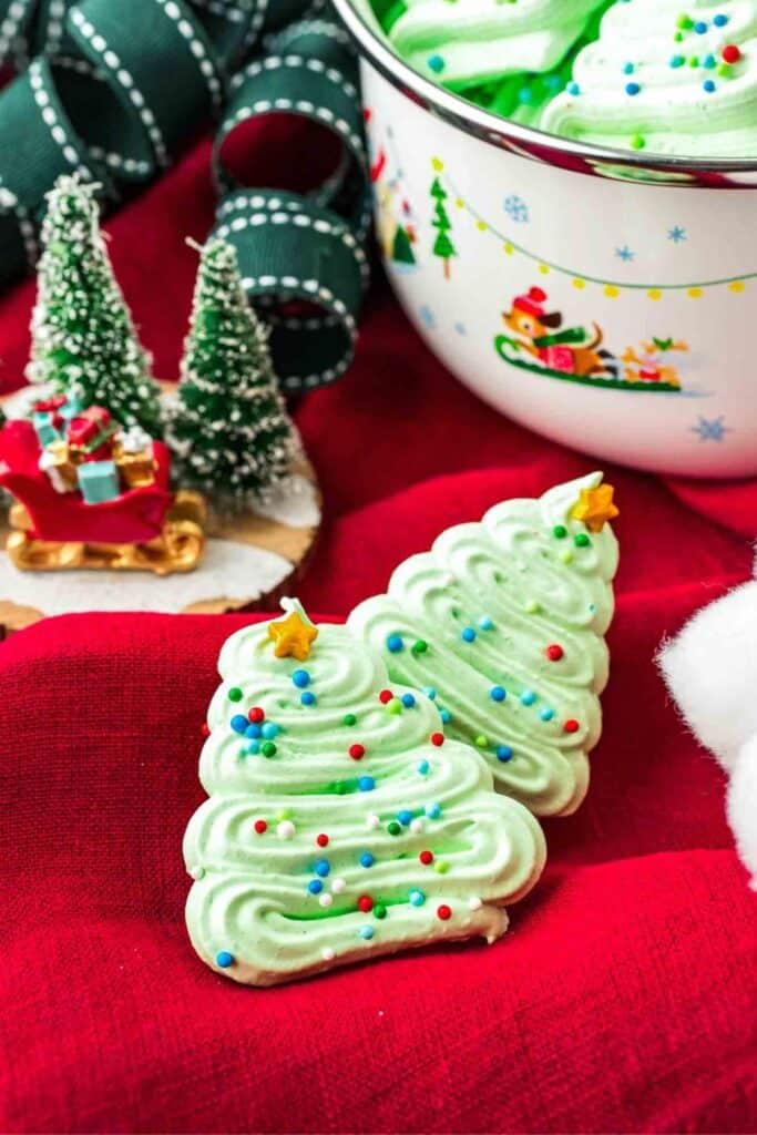 Two Christmas tree shaped meringue cookies with sprinkles on top and a candy star. 