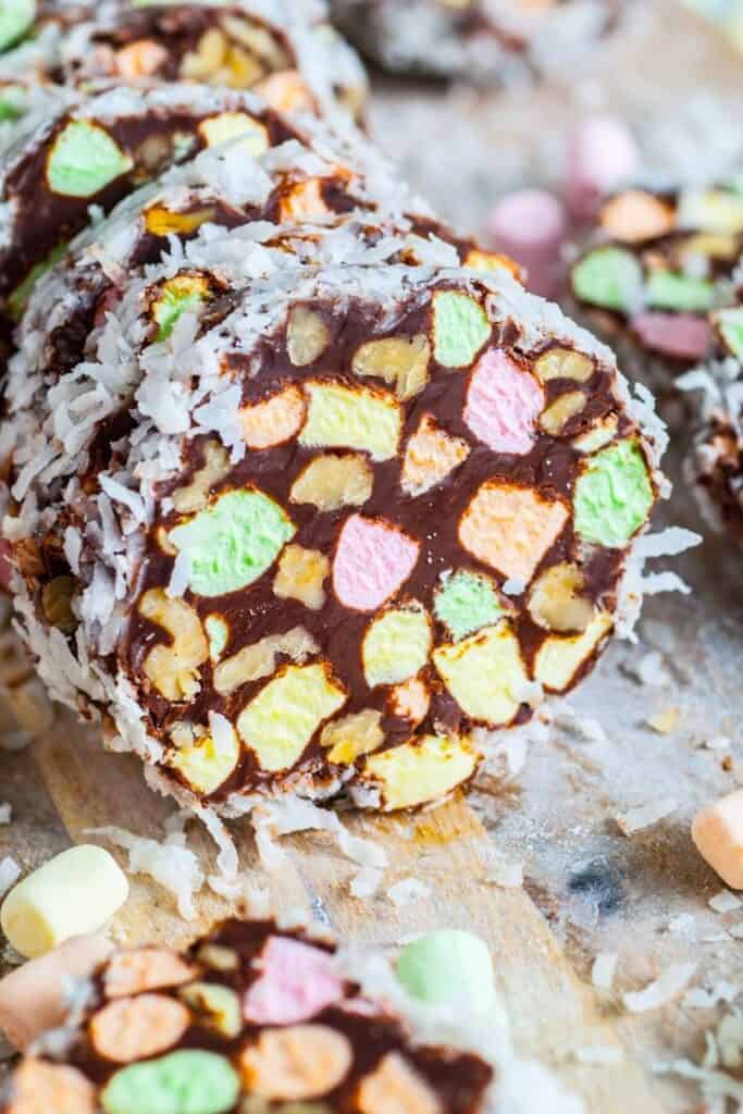 Sliced church window cookies made with colorful mini marshmallows, chocolate, chopped walnuts, and shredded coconut are arranged on a wooden surface. The stained-glass effect and festive colors make these no-bake treats a vibrant and nostalgic addition to any Christmas cookie exchange.