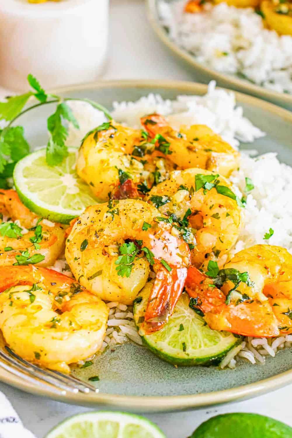 Bowl of cilantro lime shrimp served over fluffy white rice with fresh lime slices and chopped cilantro. The shrimp are coated in a buttery garlic sauce, making this recipe a bright and flavorful meal for a quick weeknight dinner.