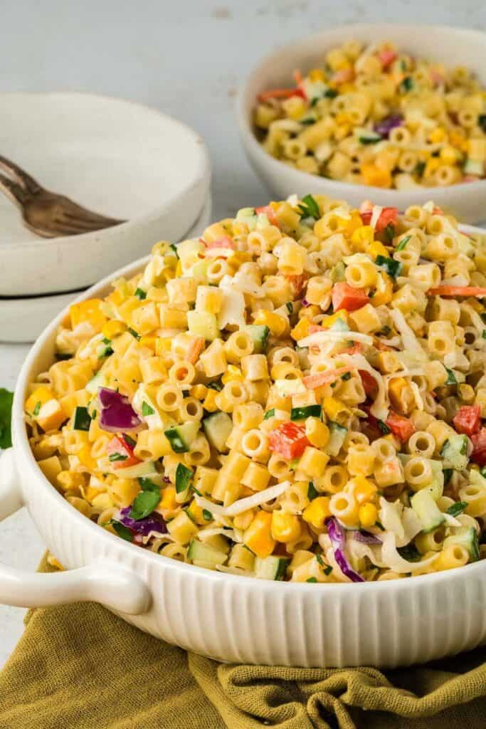 Low round ceramic dish with handles full of coleslaw pasta salad with Ditalini pasta, coleslaw mix veggies, cheddar cheese and creamy dressing.