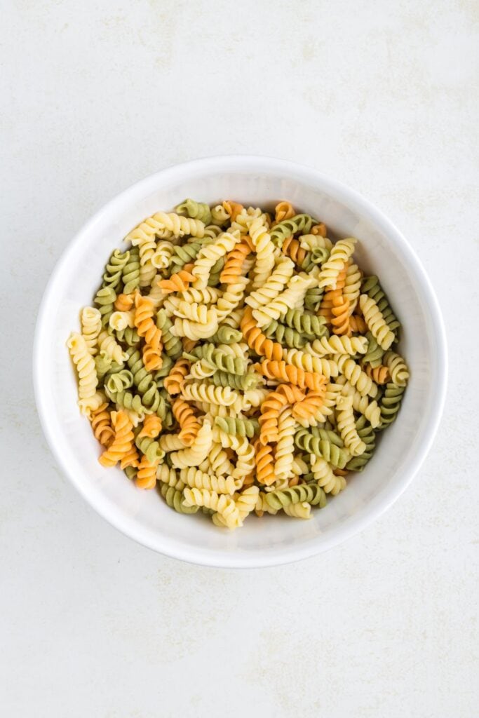 A large ceramic round bowl with cooked tri color rotini pasta inside.