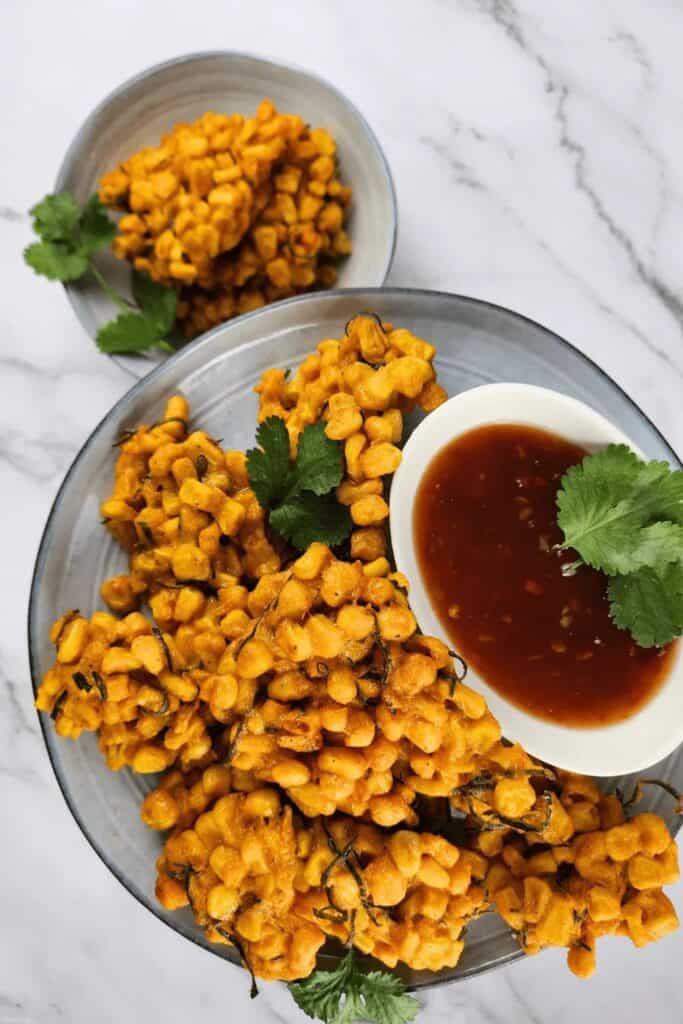 Overhead view of a plate of corn fritters, with a small bowl of red curry paste dip. 