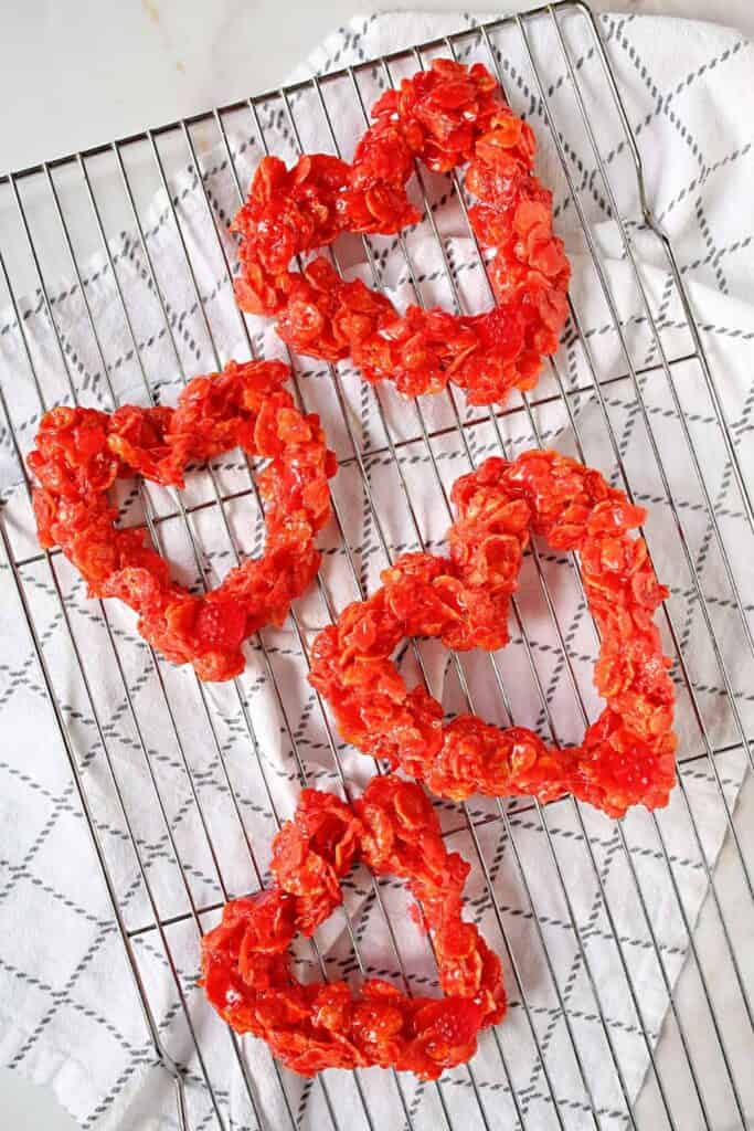  Four red cornflake hearts on a drying rack over striped tea towel.