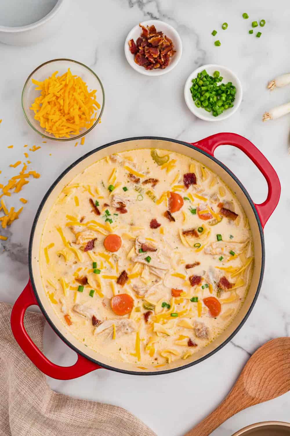 Crack chicken noodle soup with shredded chicken egg noodles carrots and celery is served in a creamy broth. The soup is topped with cheddar cheese crispy bacon and chopped green onions.