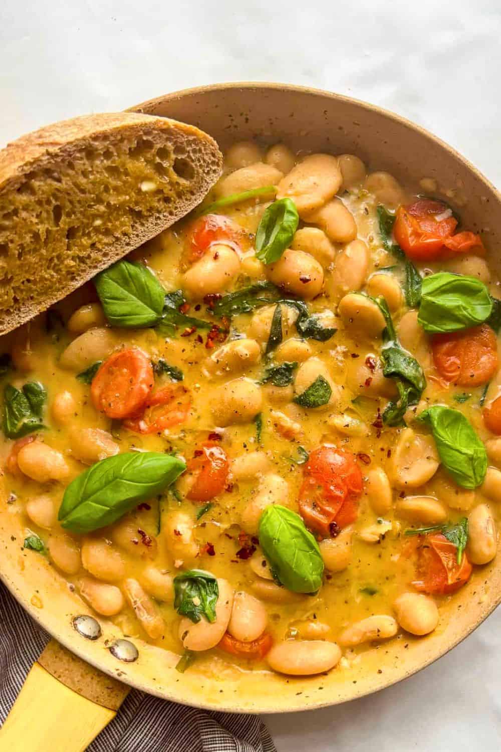 White beans simmered in a rich, creamy sauce with cherry tomatoes, spinach, fresh basil, and red pepper flakes, served with a slice of crusty bread for dipping. This creamy butter beans recipe makes a comforting one-pan meal that's perfect for lunch or dinner.