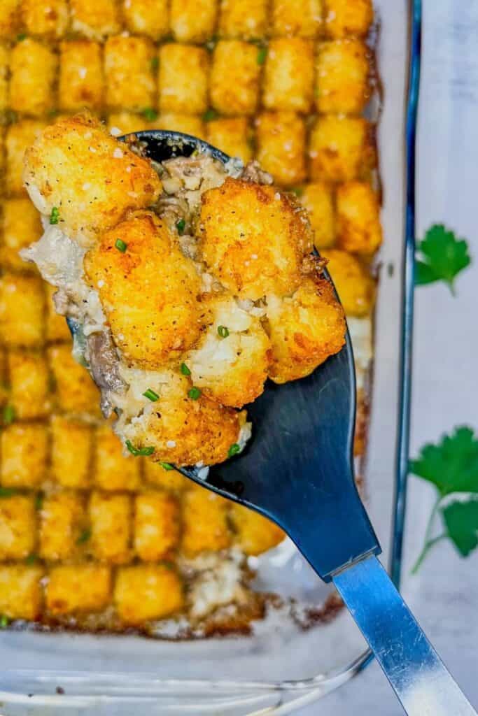 Ground beef casserole with mushrooms in a creamy sauce, topped with rows of crispy golden tater tots and sprinkled with fresh chives.