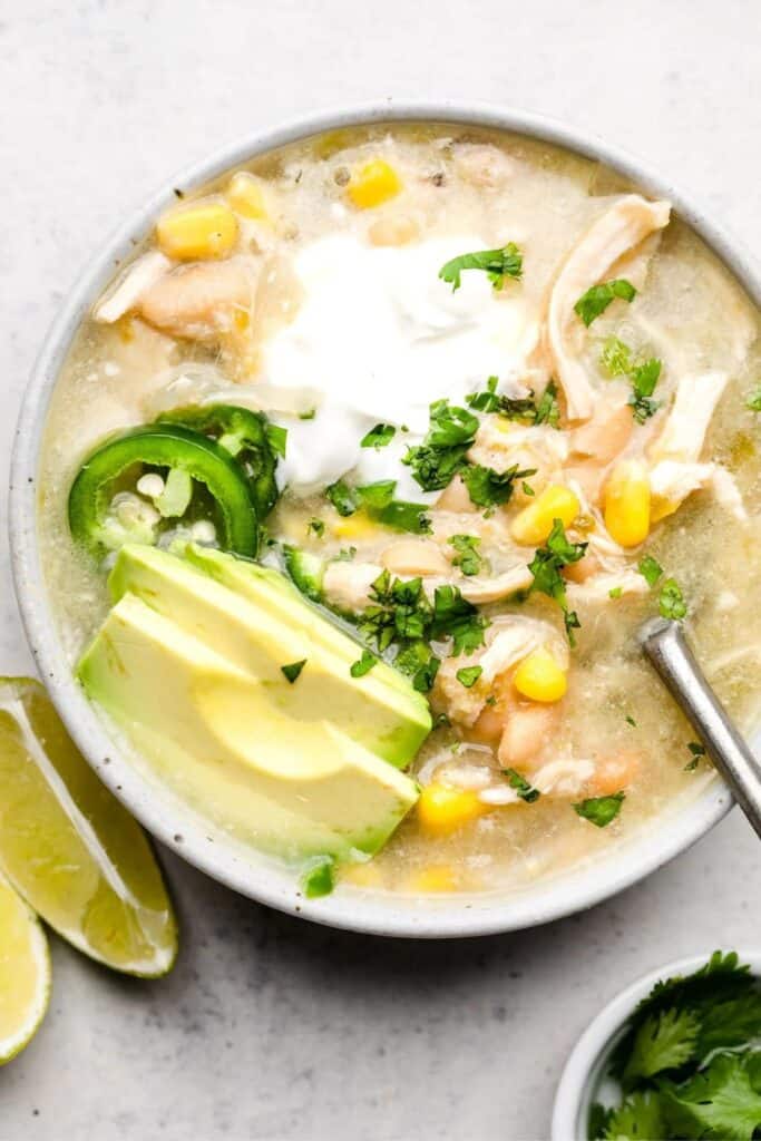 Creamy salsa verde chicken chili with corn, toppped with dollopw of sour cream, jalapeno slices and avocado slices