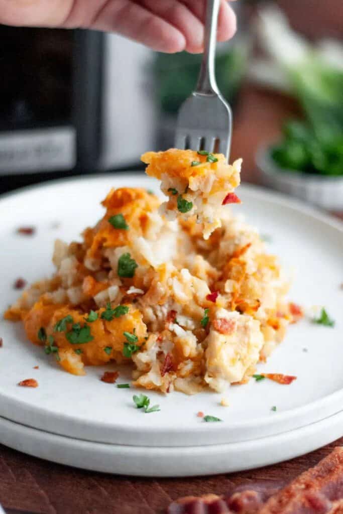 Hand holding a fork over a plate with a pile of Crockpot Chicken Bacon Tater Tot Casserole