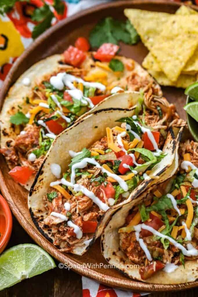 Close up of three Chicken Tacos made with corn tortillas and filled with shredded chicken, tomatoes, lettuce and cilantro.