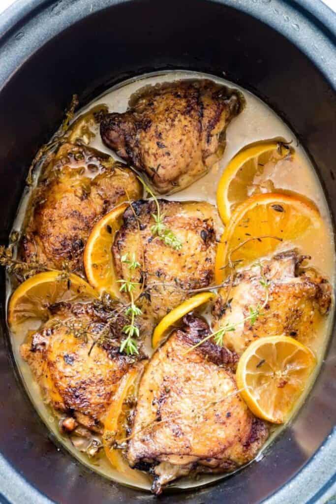 Crockpot filled with cooked chicken thighs with orange and lemon slices. 