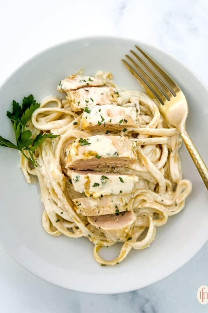 slices of crockpot garlic parmesan chicken on top of linguini pasta. 