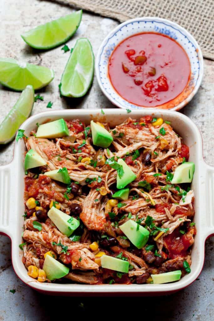 Casserole dish with crockpot salsa chicken with black beans and corn, topped with avocado cubes. 