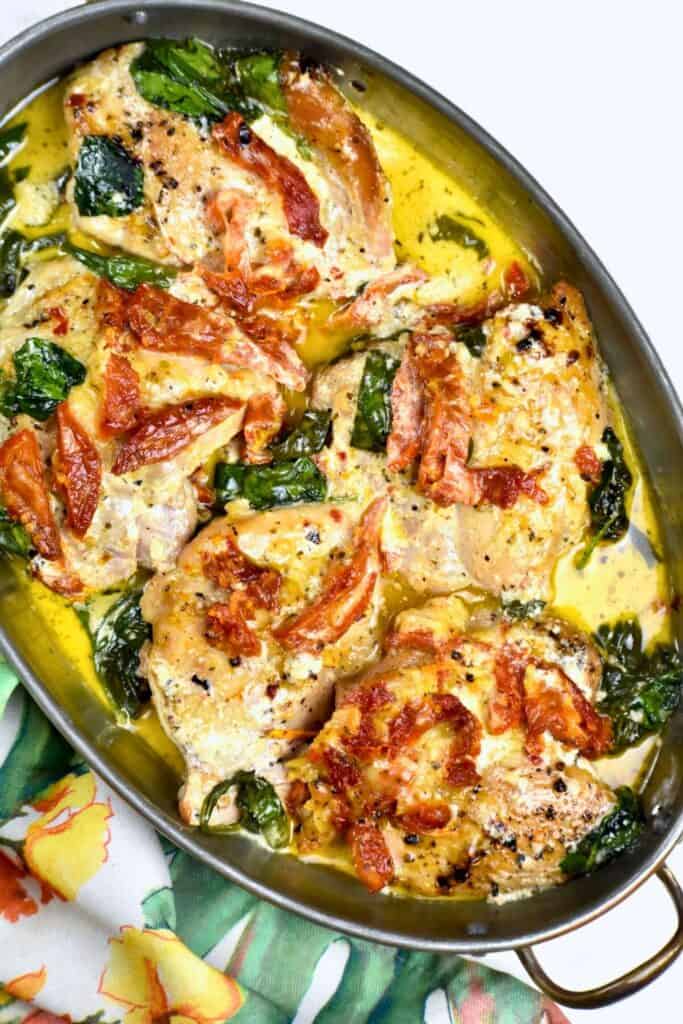 Oval metal serving dish filled with Tuscan chicken thighs, sun dried tomatoes and spinach. 