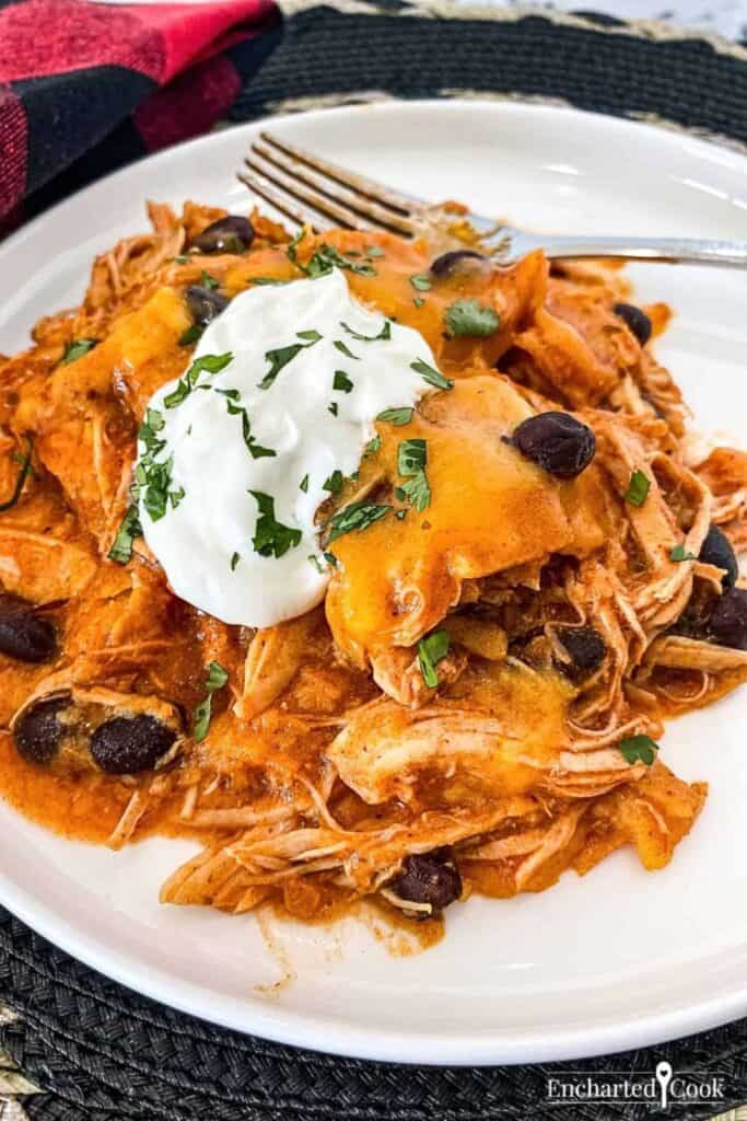 A plate full of crockpot chicken enchilada topped with cheese and sour cream.