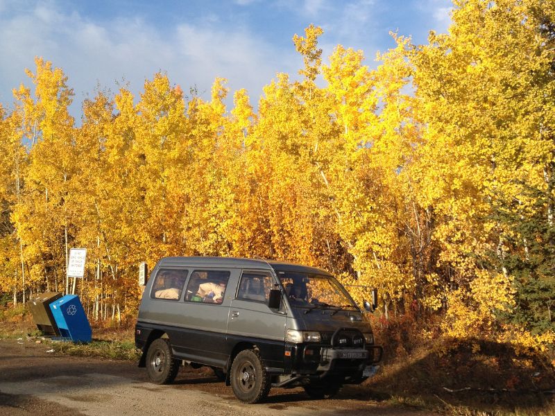 Van on side of road with fall colored leaves.
