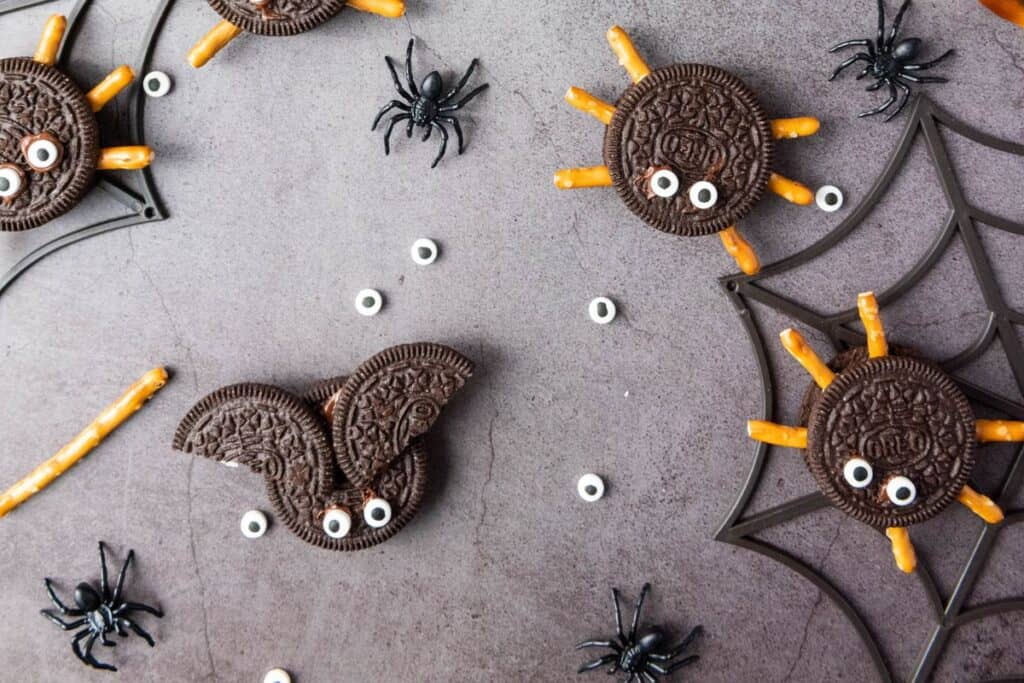 Halloween Oreo bats and spiders with candy eyes, and plastic spiders scttered around them.